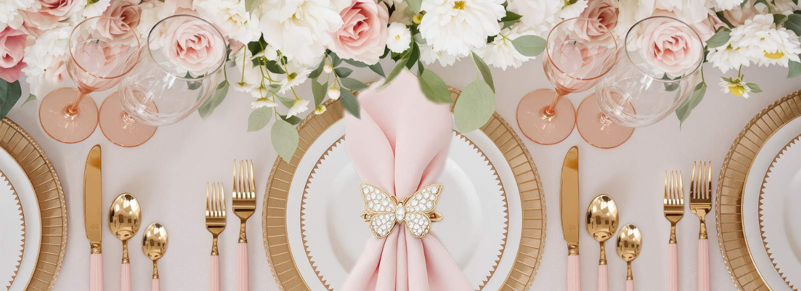 Elegant table setting with floral arrangements, pink napkins, and gold cutlery on a white tablecloth.