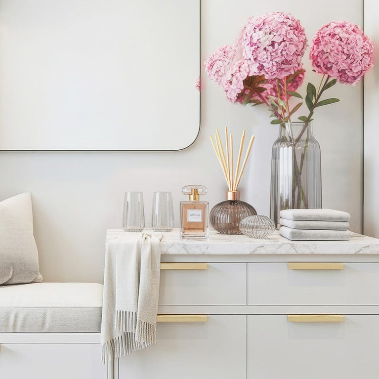 White dresser with gold handles, pink flowers, and decorative items against a light gray wall.